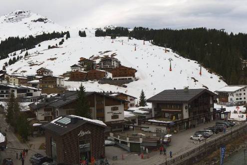 Patchy snow on the lower slopes of Lech, Austria, with village in the foreground – Weather to ski – Snow report, 29 March 2024