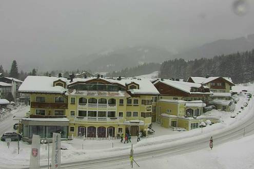 Cloudy skies above the buildings of Hinterthal, Austria, with views through the clouds towards the trees and ski slopes beyond the village centre – Weather to ski – Snow forecast, 21 January 2022