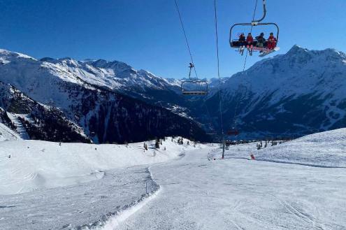 Blue skies over snowy piste in La Rosière, France, with chairlift above the slope and seated skiers – Weather to ski – Snow forecast, 28 January 2022