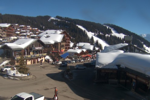 Blue skies over the resort centre of Les Saisies, France, with view towards the snow-covered ski slopes with chalet style buildings in the foreground – Weather to ski – Snow forecast, 4 February 2022