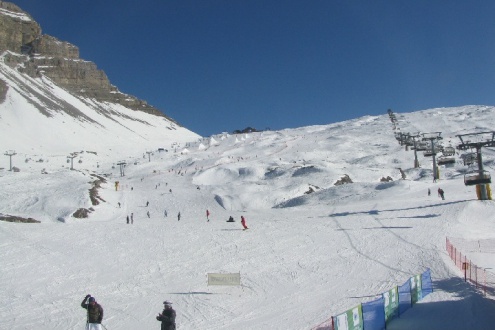 Blue skies over snow-covered pistes in Madonna di Campiglio, Italy, with skiers descending the slope and a chairlift to the right of the picture – Weather to ski – Snow forecast, 4 February 2022