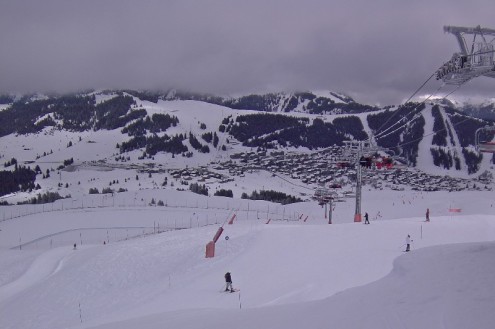 View over snowy ski slopes with skier under cloudy skies looking over the valley to Les Saisies, France, with mountains in the background and chairlift to the right – Weather to ski – Snow report, 20 January 2022