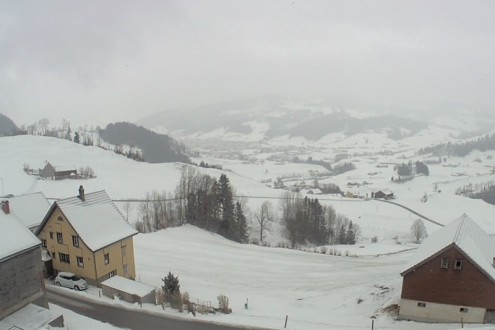 Cloudy skies and view across the snowy valley in Appenzell, Switzerland, with houses in the foreground – Weather to ski – Snow report, 20 January 2022