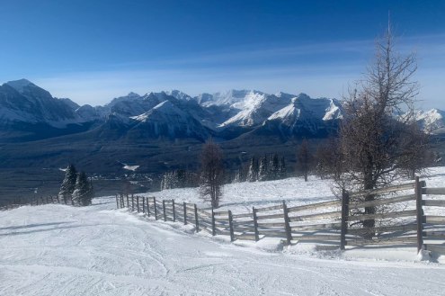 Snowy ski slopes with fence in the foreground and panoramic mountain views in the background with clear blue skies in Banff/Lake Louise, Canada – Weather to ski – Snow report, 20 January 2022