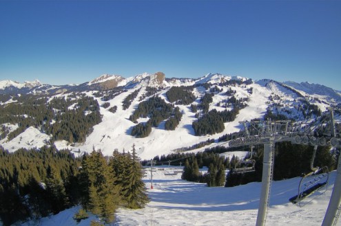 Blue skies above a chairlift rising from the valley below with panoramic snowy mountain scenery in Les Gets, France – Weather to ski – Snow report, 28 January 2022