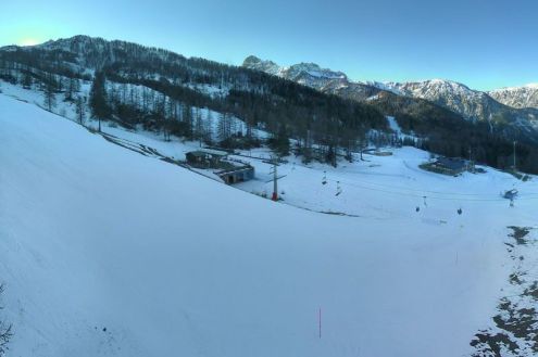 Sunrise behind the tree-covered mountain in Bardonecchia, with snowy pistes in the foreground – Weather to ski – Snow report, 28 January 2022
