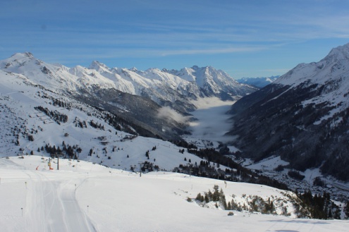 Panoramic snowy mountain view from the pistes above St Anton, Austria, over the valley below with blue skies with streaks of high cirrus cloud above, and the village in the valley – Weather to ski – Snow report, 3 February 2022