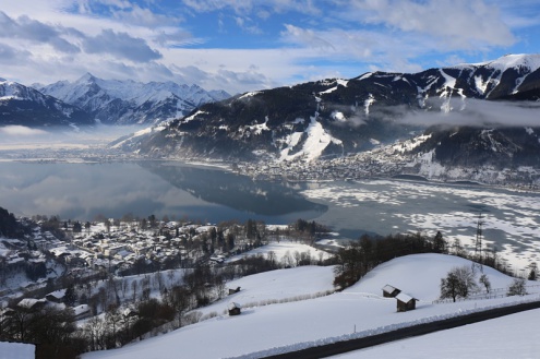View across lake at Zell-am-See with panoramic snowy mountain scenery – Weather to ski – Snow report, 17 February 2022