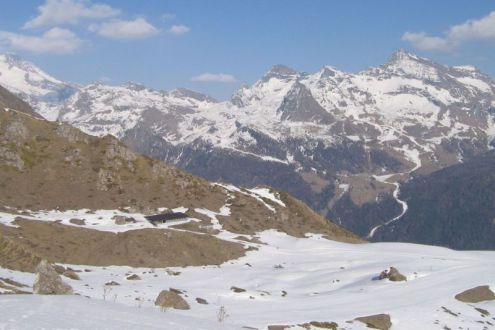 Panoramic snowy mountain view, with building in the distance, rocky terrain and blue skies in Antagnod, Monte Rosa region, Italy – Weather to ski – Snow report, 25 March 2022