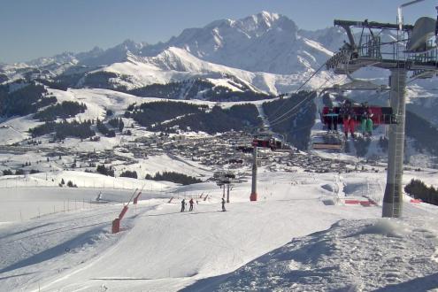 View down the slopes in Les Saisies, France, with panoramic mountain scenery and skiers on chairlift in the foreground – Weather to ski – Snow report, 10 February 2023