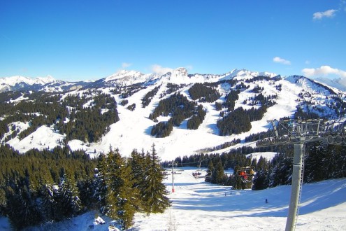 Blue skies over panoramic mountain scenery in Les Gets, France, with skiers on chairlift in the foreground – Weather to ski – Snow report, 2 February 2023
