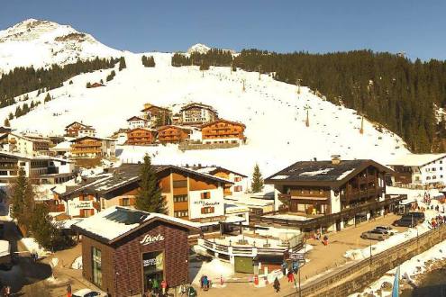 View over the village of Lech, with blue skies above snow-covered ski slopes in the distance – Weather to ski – Snow report, 4 March 2023