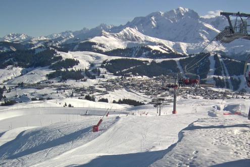 Panoramic view of snow-covered ski slopes, skiers on a chairlift, and over the village below in Les Saisies, France – Weather to ski – Snow report, 3 February 2024