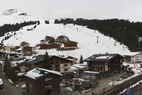 Plenty of snow on the ski slopes of Lech, Austria, with view over the village towards the ski slopes and lifts, and cloudy skies above – Weather to ski – Snow report, 15 March 2024