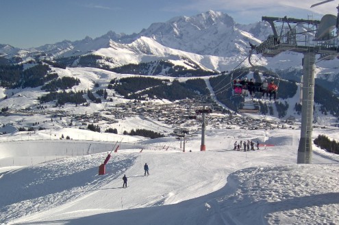 Blue skies over snowy ski slopes with panoramic mountain views and skiers sitting on chair lifts in the foreground in Les Saisies, France – Weather to ski – Today in the Alps, 17 January 2022
