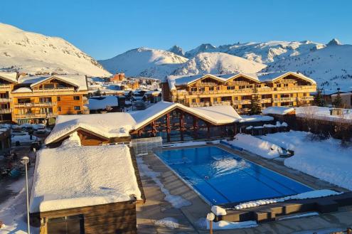 View of outdoor pool at the leisure centre in Alpe d’Huez, with snowy mountains in the background – Weather to ski - Our blog: Alpe d’Huez – one of the best all-round ski resorts in the Alps?