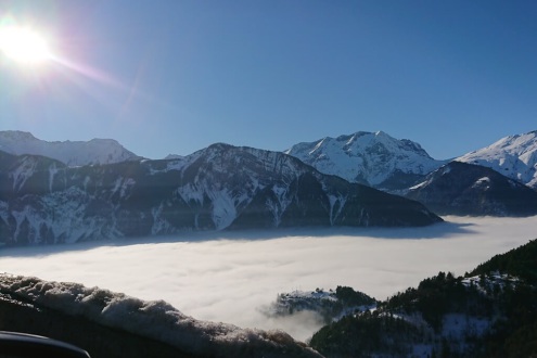 View over the valley of Bourg d’Oisans from the approach road to Alpe d’Huez, with bright blue sunny skies but a sea of thick cloud covering the valley below, on 16 December 2021 - Weather to ski – Our blog: Alpe d’Huez – one of the best all-round ski res