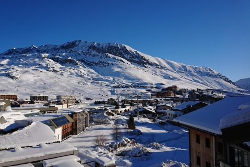 View towards the Bergers district of Alpe d’Huez from the balcony of the Chalet des Neiges apartments with panoramic views of the snowy mountains in the background and resort buildings in the foreground, on 17 December 2021 - Weather to ski – Our blog: Al