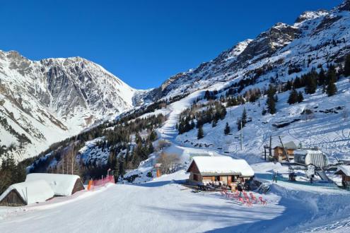 Pistes in the Montfrais sector above Vaujany with blue skies, snowy mountain views and chalet style buildings with deckchairs on 19 December 2021 – Weather to ski – Our blog: Alpe d’Huez – one of the best all-round ski resorts in the Alps?