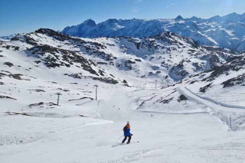 View of the Sarenne black run part way towards the Gorge with sweeping panoramic mountain views, sunny skies and empty slopes apart from one skier in the foreground, on 21 December 2021 – Weather to ski - Our blog: Alpe d’Huez – one of the best all-round 