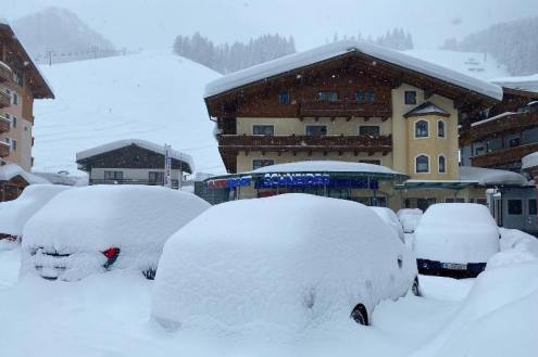 Deep snow covering parked cars in the village of Zauchensee, Austria, with chalet-style buildings in the background – Weather to ski – Today in the Alps, 2 February 2022