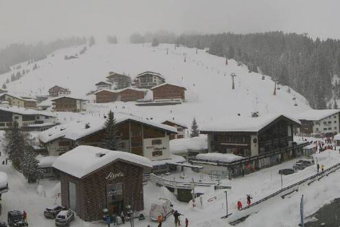 Cloudy weather and snow falling in Lech, Austria, with view across the resort centre and chalet-style buildings to the snow-covered ski slopes behind – Weather to ski – Today in the Alps, 7 February 2022