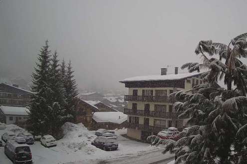 Cloudy weather in Les Gets, France, with view of snow-covered road, cars and chalet-style buildings – Weather to ski – Today in the Alps, 11 February 2022