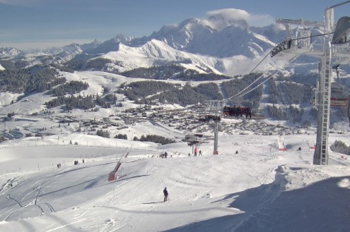 View over snow-covered ski slope looking down towards the ski resort of Les Saisies, France, with chairlift and skiers in the foreground – Weather to ski – Today in the Alps, 22 February 2022