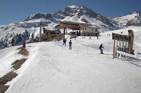 View of snow-covered piste in the ski resort of Aussois, France, with skiers standing a lift queue and blue skies above – Weather to ski – Today in the Alps, 28 February 2022