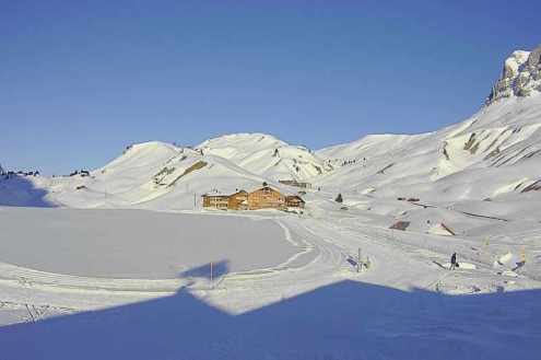 Snow covered mountain landscape in the ski resort of Warth-Schröcken, Austria, with chalet-style building in the distance and blue skies above – Weather to ski – Today in the Alps, 1 March 2022
