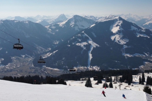 Skiers on the pistes in Ski Welt, Austria with chairlift above to the left and panoramic mountain views – Weather to ski – Today in the Alps, 25 March 2022