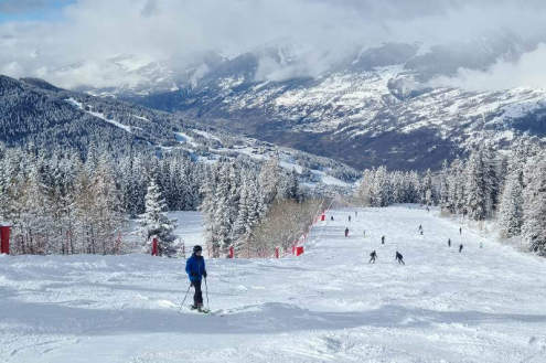 Snowy tree-lined ski slope with skiers, cloudy skies and panoramic valley views - Weather to ski – Our blog: Top 5 pistes in Les Arcs