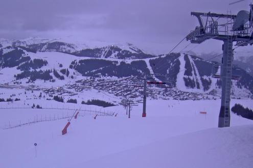 Cloudy weather at dawn in Les Saisies, France, looking down the ski slope to the valley below and across to the ski slopes with ski lift pylons in the foreground – Weather to ski – Today in the Alps, 21 December 2022