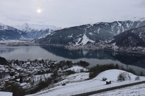 Sun trying to break through the clouds over the lake in Zell-am-See, with view towards the ski slopes – Weather to ski – Snow report, 1 December 2023