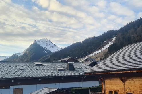 View of ski slopes beyond the rooftops of buildings in Morzine, France – Weather to ski – Today in the Alps, 11 March 2024