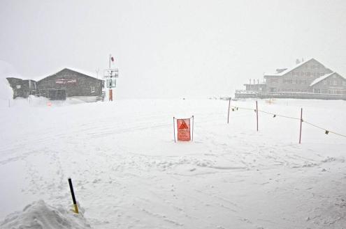 Heavy snow falling on the ski slopes at high altitude in Engelberg, with view of two mountain buildings and thick cloud – Weather to ski – Today in the Alps, 18 March 2024