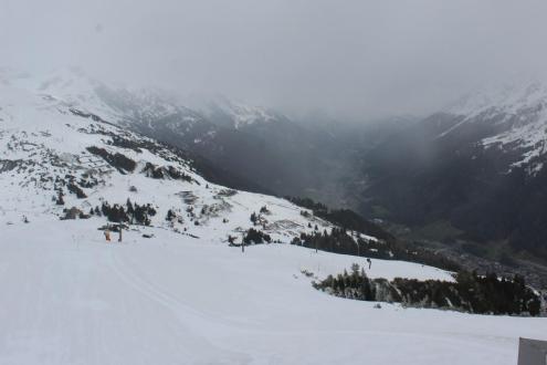 Low cloud and snow falling on the ski slopes of St Anton, Austria, with view over snow-covered slopes towards the valley below – Weather to ski – Today in the Alps, 16 April 2024
