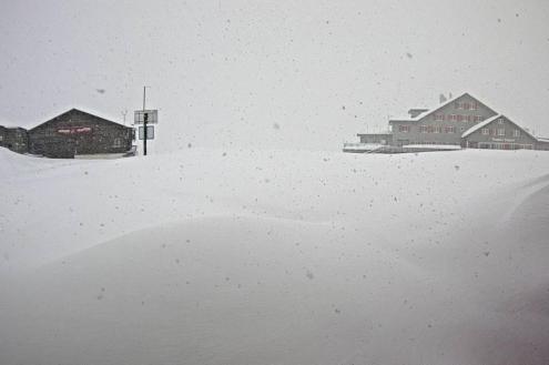 Huge piles of accumulated snowfall on the mountainside with more snow still falling in Engelberg, Switzerland, with two mountain buildings in the background – Weather to ski – Today in the Alps, 20 April 2024