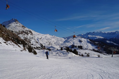 Skier standing on empty wide snow-covered ski slope with panoramic mountain views and ski-lift above, in Bettmeralp, Aletsch Arena, Switzerland – Weather to ski – Today in the Alps, 15 December 2025