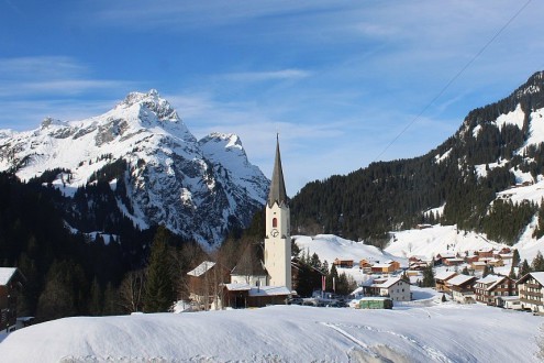 Blue skies over the chapel and village buildings in snowy Warth-Schröcken, Austria – Weather to ski – Today in the Alps, 14 January 2026