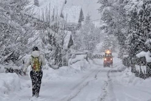 Heavy snow falling in Courmayeur, Italy, with person walking along a snow-covered road past chalet-style buildings – Link to Weather to ski's full "Today in the Alps" report on weather and snow in the Alps on 10 February 2026