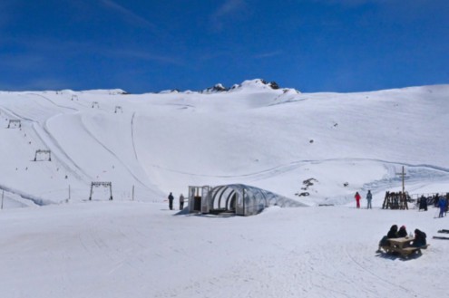 Blue skies over the ski slopes in Les 2 Alpes, with a beginners’ covered rolling carpet style lift in the foreground – Weather to ski – Today in the Alps, 20 April 2026