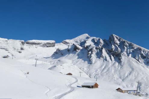 Blue skies above the freshly snow-covered slopes of the First sector above Grindelwald in the Jungfrau Region, with ski lift in front of mountains, on 22 October 2026